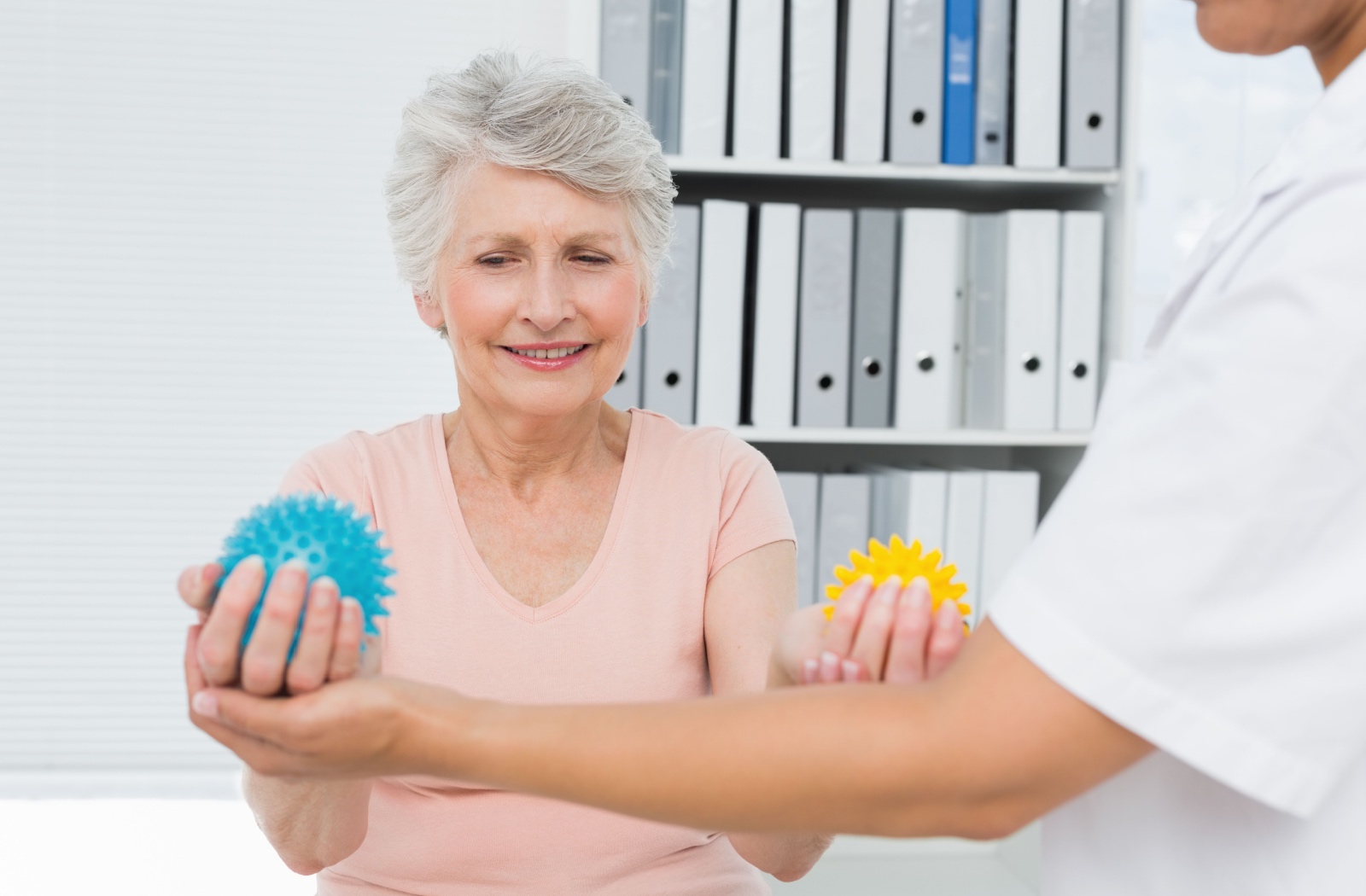 An older adult doing hand exercises with stress balls while being accompanied by a physical therapist