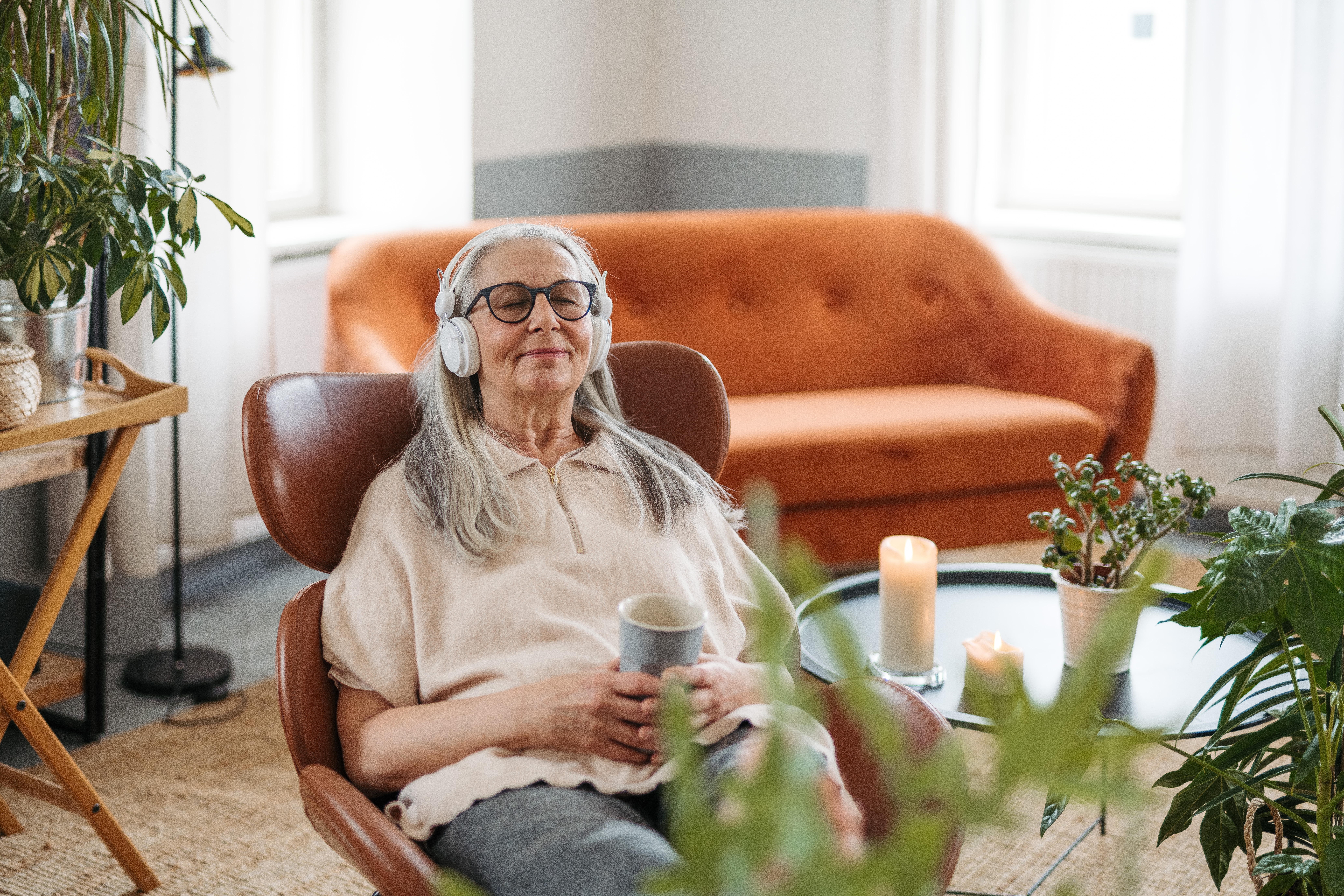 A woman with dementia relaxes on a chair and closes her eyes while listening to music through headphones.
