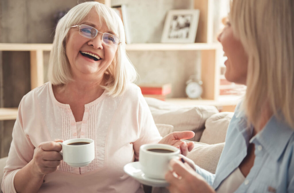 An older adult woman and her adult daughter enjoy a cup of coffee while conversing on a couch in an independent living community.