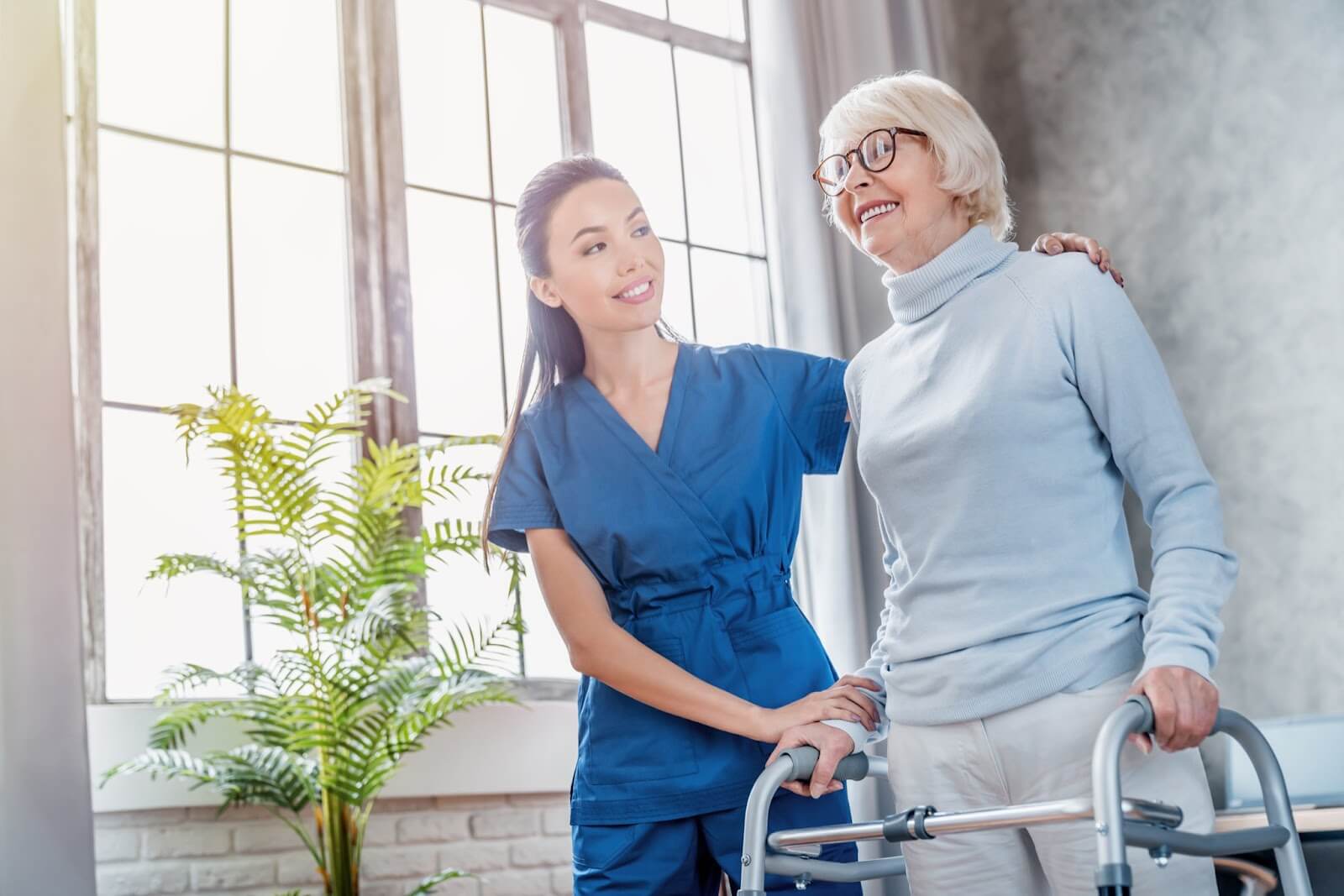 A young personal care home caregiver assisting an older adult with walking.