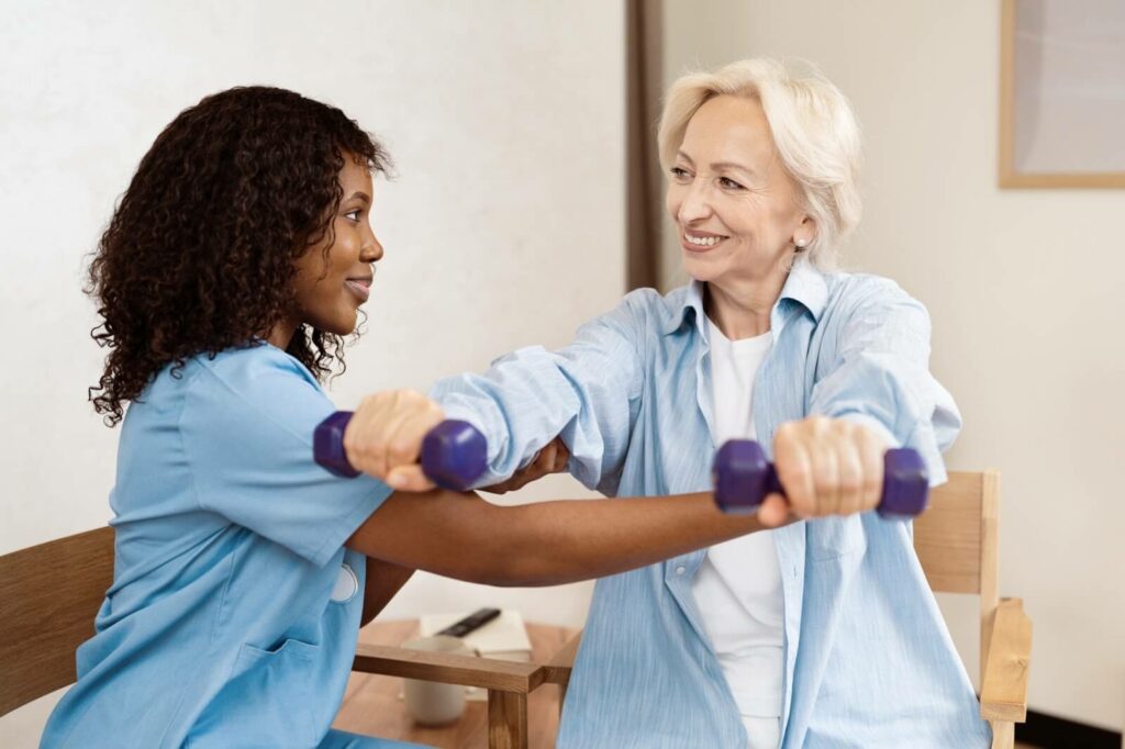 A young caregiver assisting a mature woman with arm exercises.