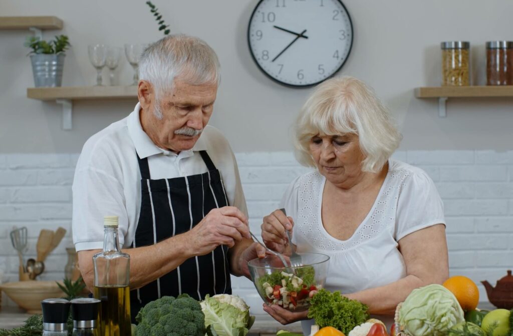 Older adult couple preparing a salad together in a kitchen.