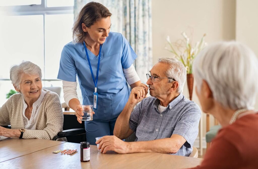 Caregiver assists elderly man taking medication during a group activity.