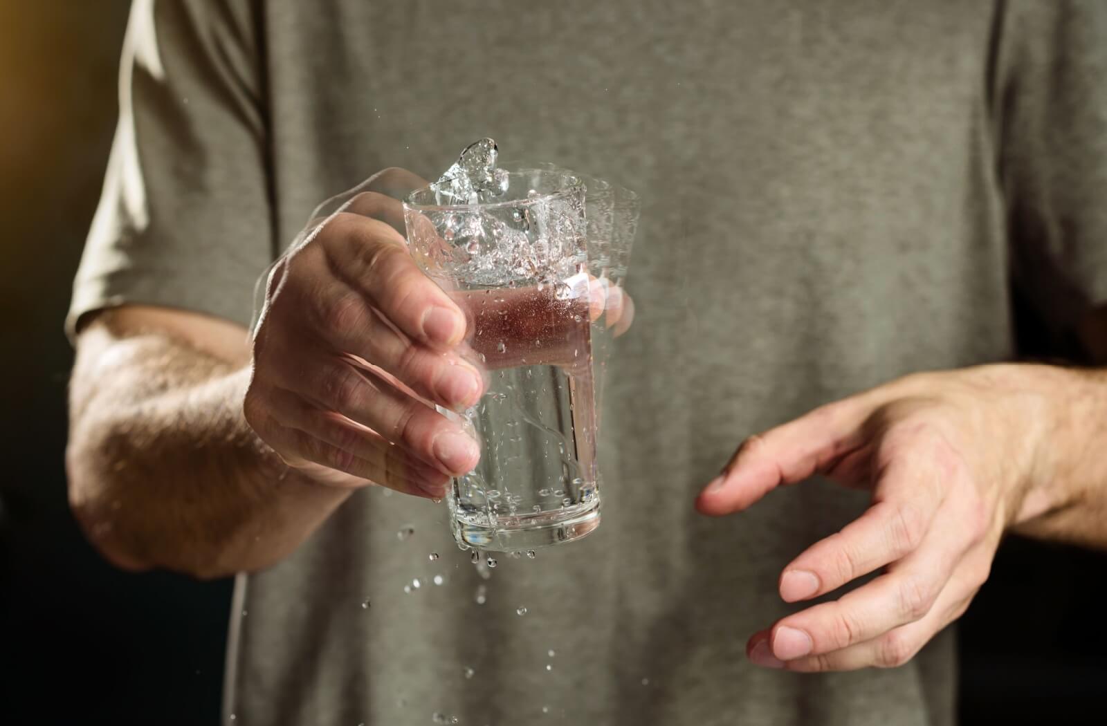 A person with Parkinson's disease holds a glass of water, their hand shaking it uncontrollably.