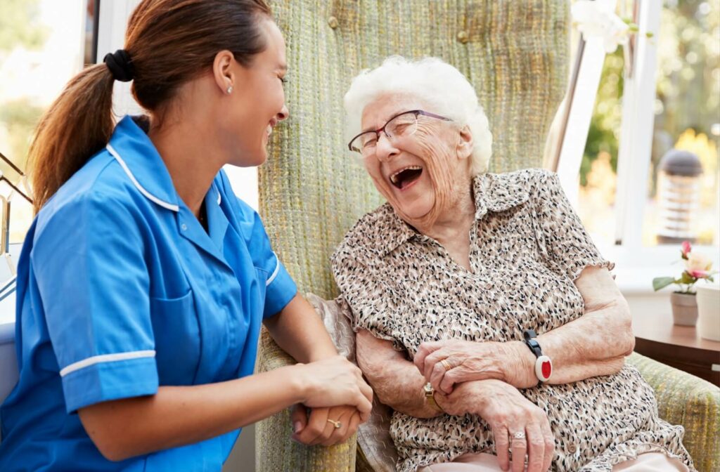 An older adult laughs with a young assisted living caregiver.
