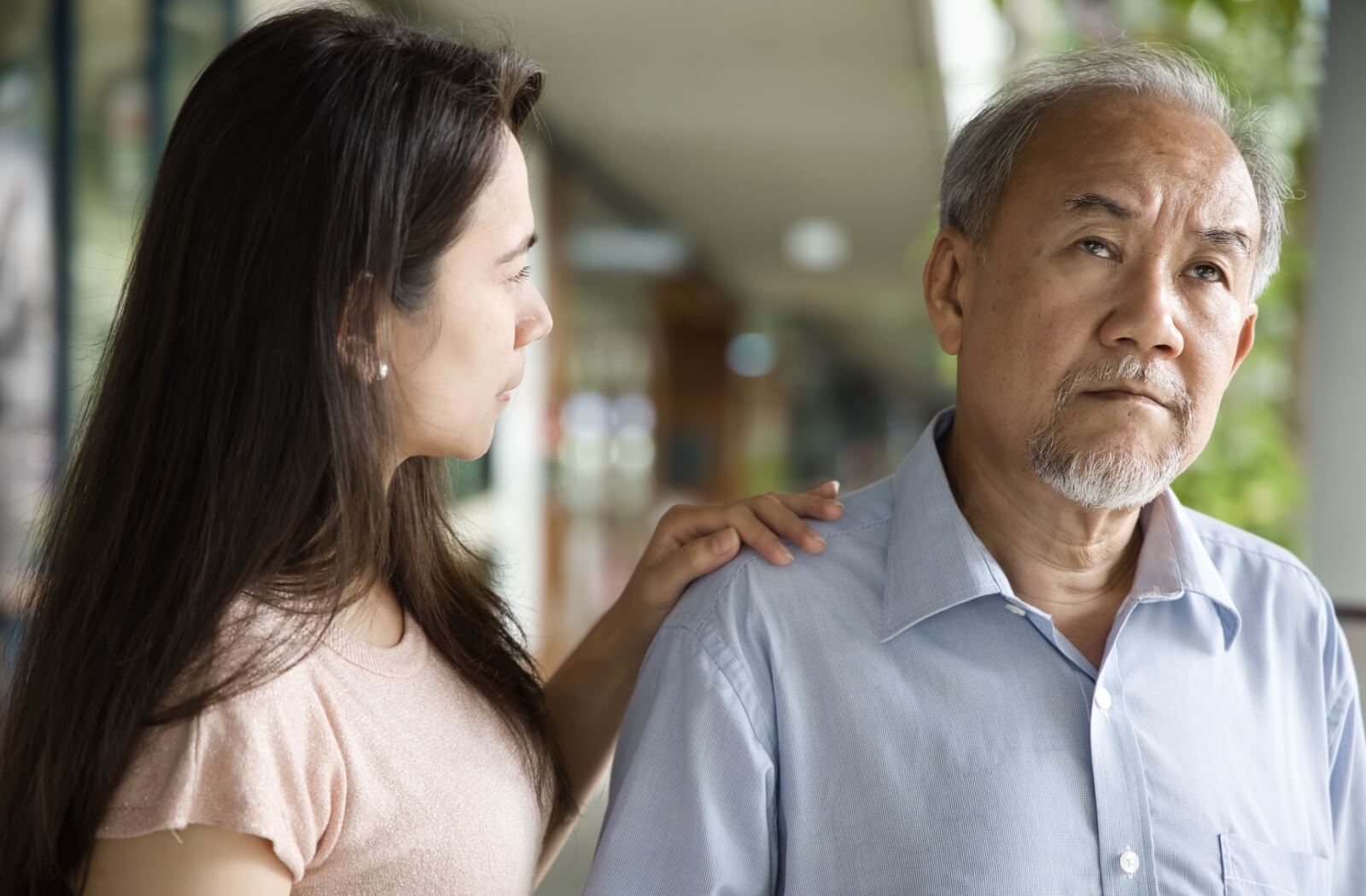 A frustrated older adult looks off into the distance as their daughter tries to comfort them.
