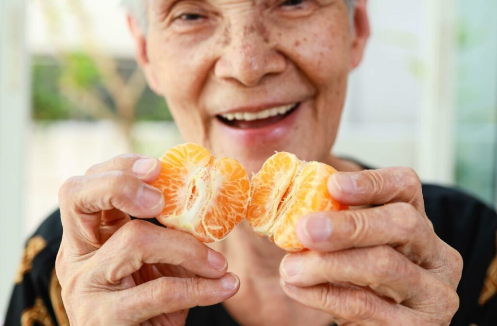 A close-up shot of a cheerful older woman holding a mandarin orange.