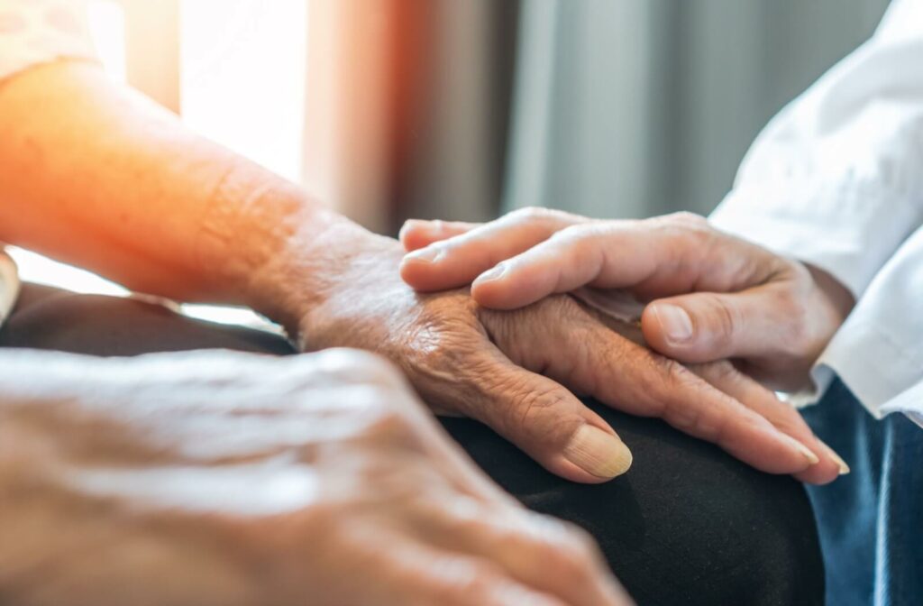 A close-up image of a caregiver touching an older adult's hand to reassure them in memory care.