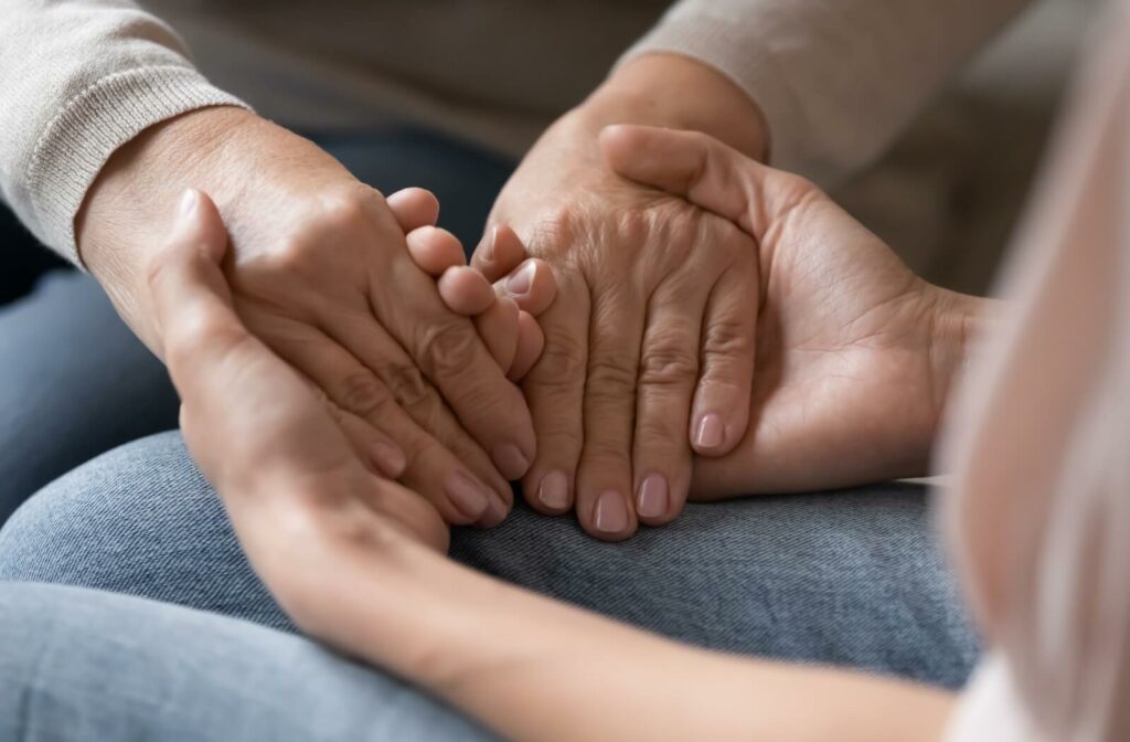An adult child holds their older parent's hands to reassure them during a conversation about dementia