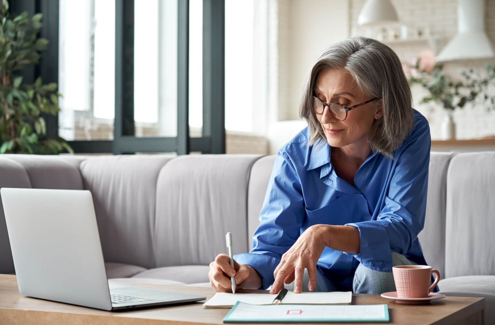 An older adult doing research on a laptop and taking notes to see if they are qualified for personal care.